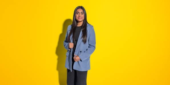 Trisha steht im Blazer und schaut seitlich in die Kamera.