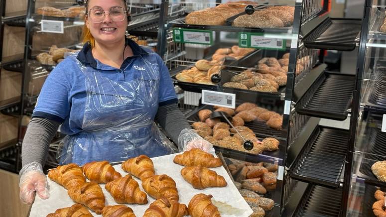 Bianca steht vor dem Backshop mit einem Blech voll Croissants.