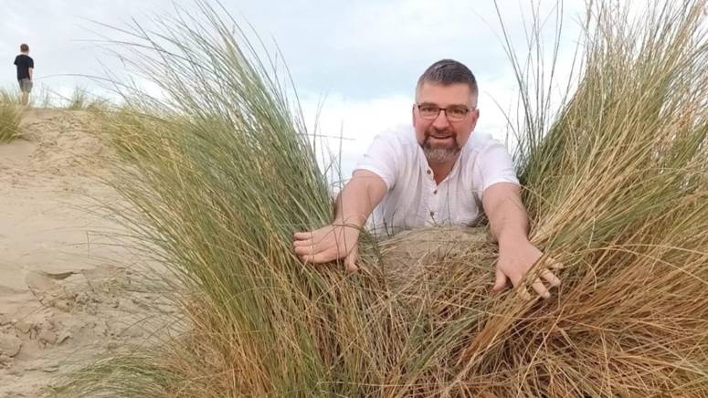 Filialleiter Marco liegt im Sand und schaut durch das hohe Gras.
