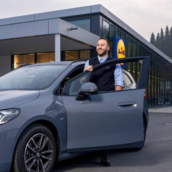 Der Filialleiter steht am Auto und lächelt.