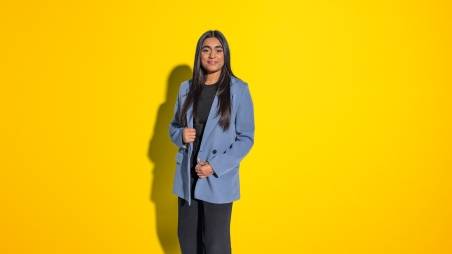 Trisha steht im Blazer und schaut seitlich in die Kamera.